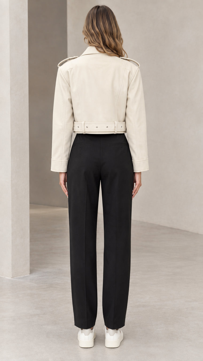 Back view of woman wearing cream cropped faux leather jacket showing waistband and shoulder seams