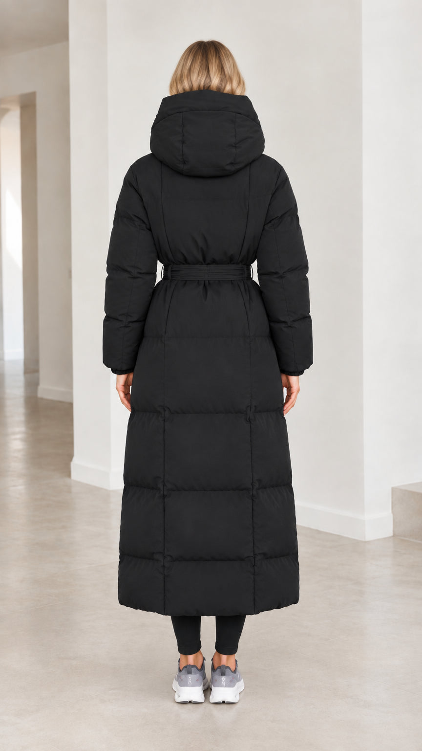 Back view of model wearing black hooded maxi puffer coat cinched at waist