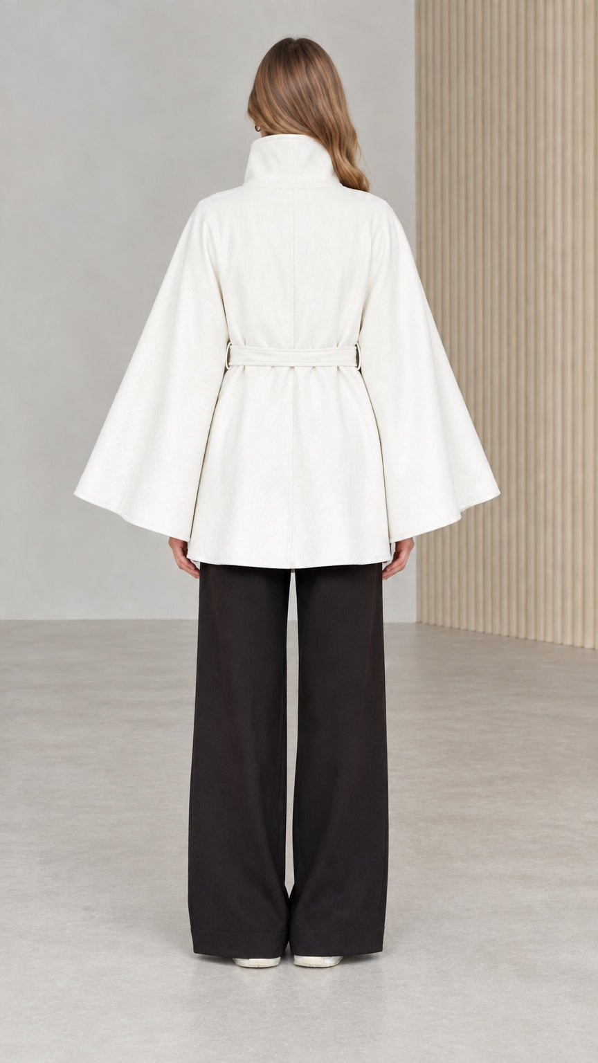 Back view of model wearing white high neck cape coat with belt