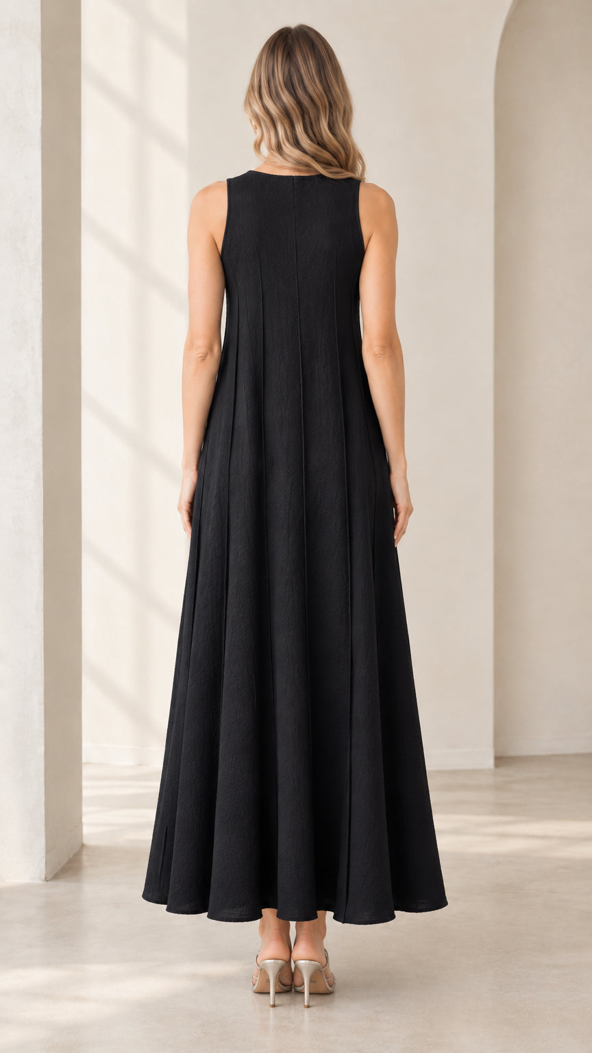 Back full-length view of woman wearing black sleeveless maxi dress showing vertical seam detailing