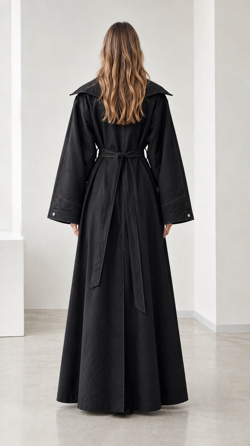 Back view of woman wearing full-length black duster coat with tie waist