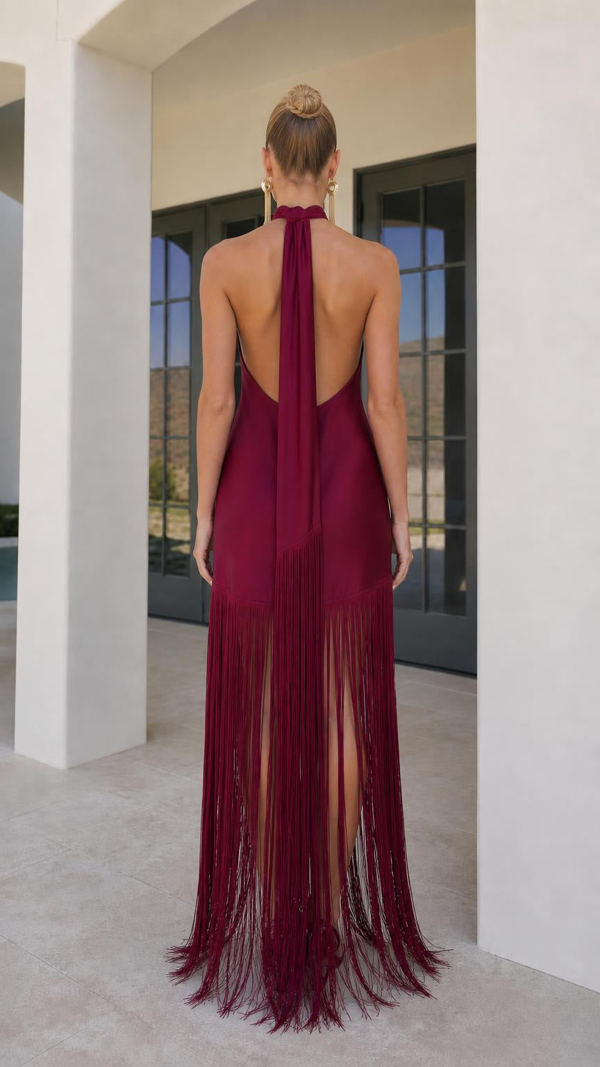 Model wearing burgundy satin halter fringe maxi dress back view