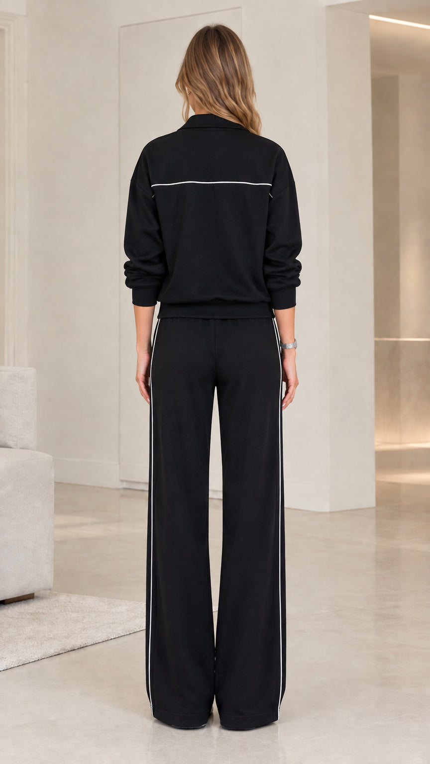 Back view of model wearing black zip-up track jacket and straight wide-leg trousers