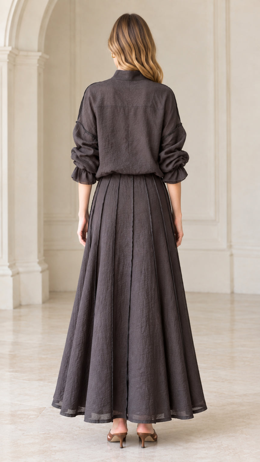 Back view of woman wearing charcoal grey long sleeve top and pleated maxi skirt