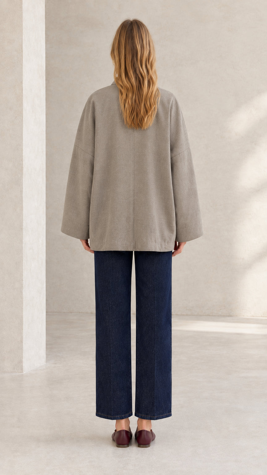 Back view of woman wearing taupe minimalist jacket and wide navy trousers
