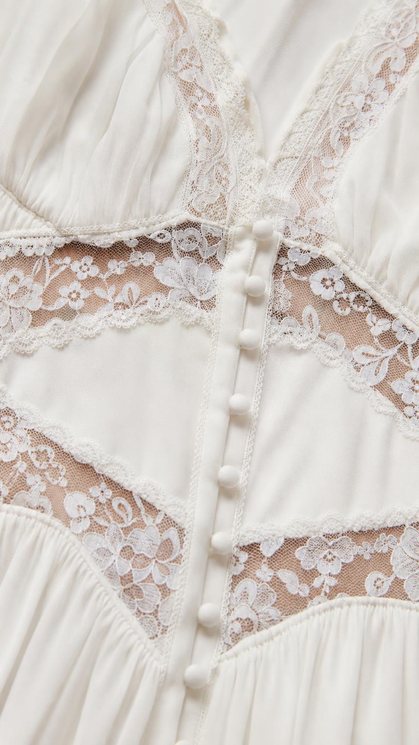 Close-up detail of lace inserts and front buttons on white dress