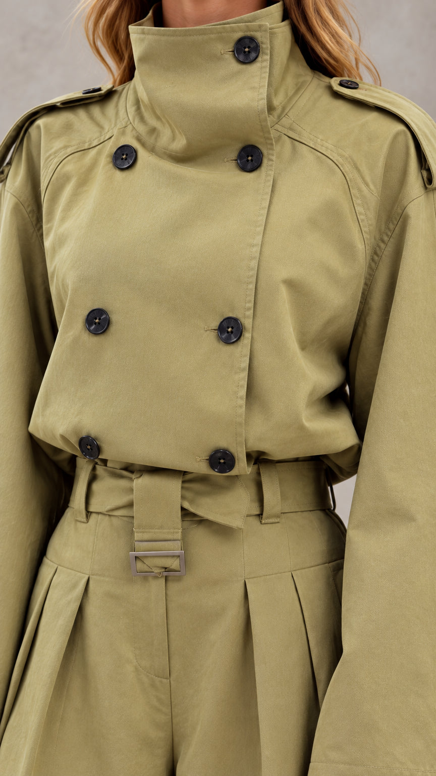 Close-up detail of high collar, double-breasted buttons, shoulder tabs, and belted waist