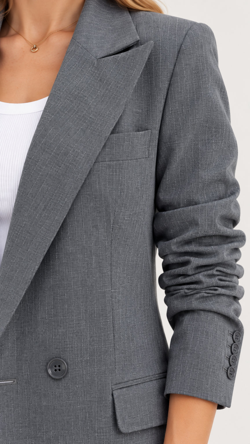Close-up detail of grey coat showing sharp peak lapel, chest pocket, and cuff buttons