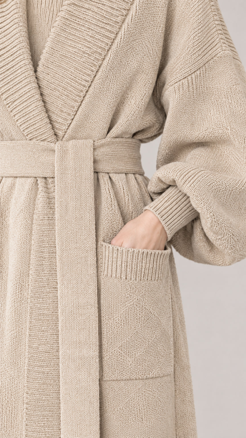 Close-up detail of textured knit fabric, ribbed lapel, tie belt, and pocket on beige cardigan