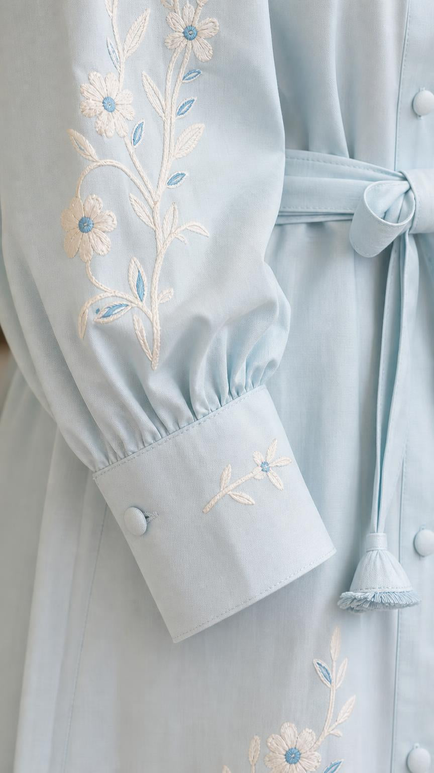 Close-up of embroidered sleeve cuff and belt on light blue dress