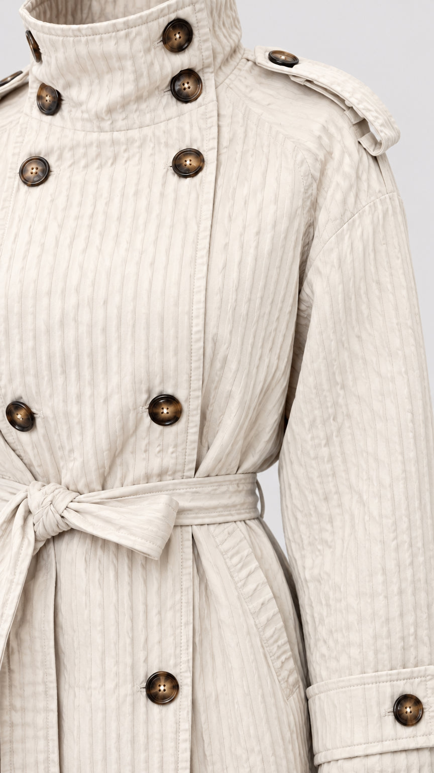Close-up detail of cream textured short coat showing double-breasted buttons, collar, and belt
