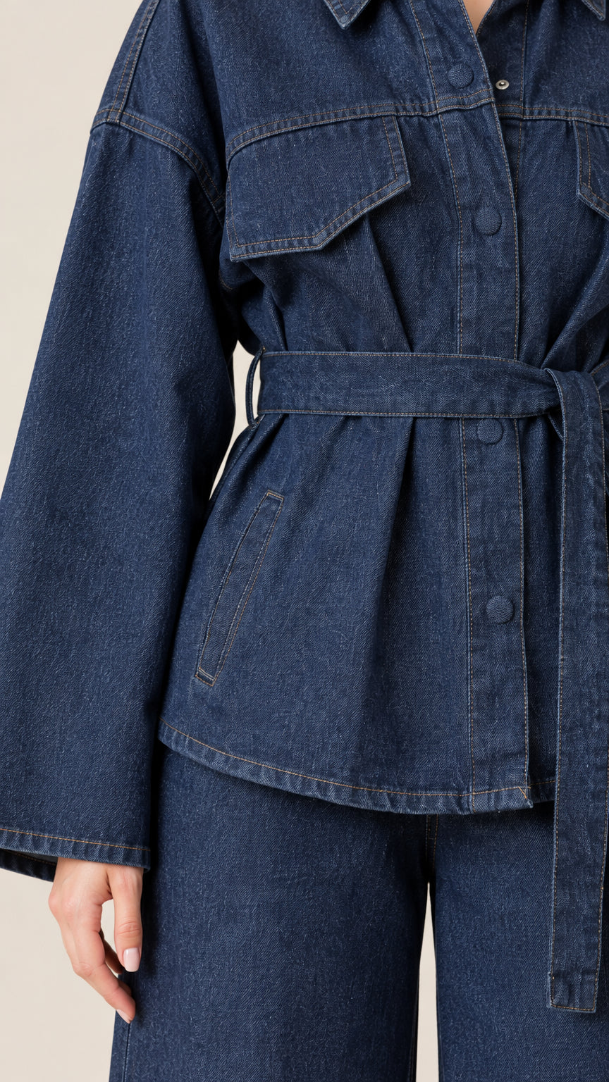 Close-up detail of dark blue denim utility jacket with pockets and tie belt