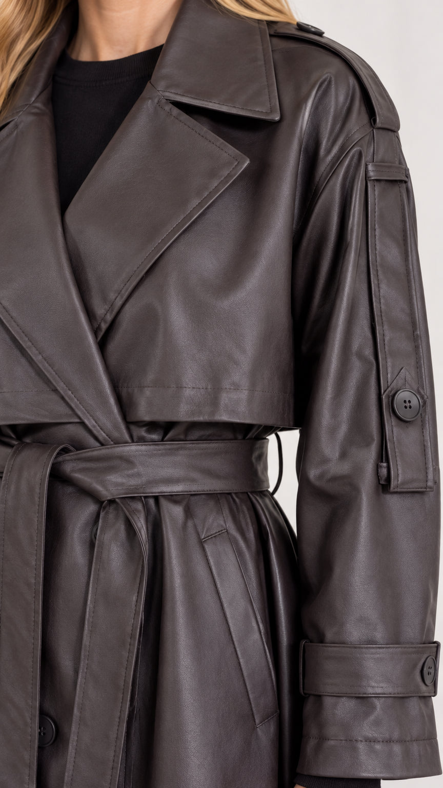 Close-up detail of lapel collar and sleeve tab on dark brown faux leather coat