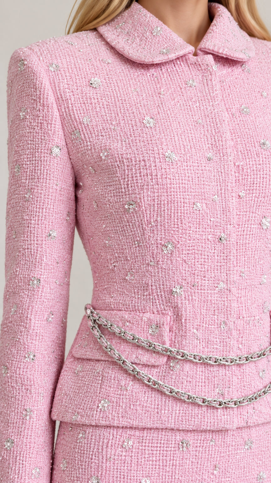 Close-up detail of textured pink bouclé tweed fabric with rhinestone sparkles and chain pocket accent