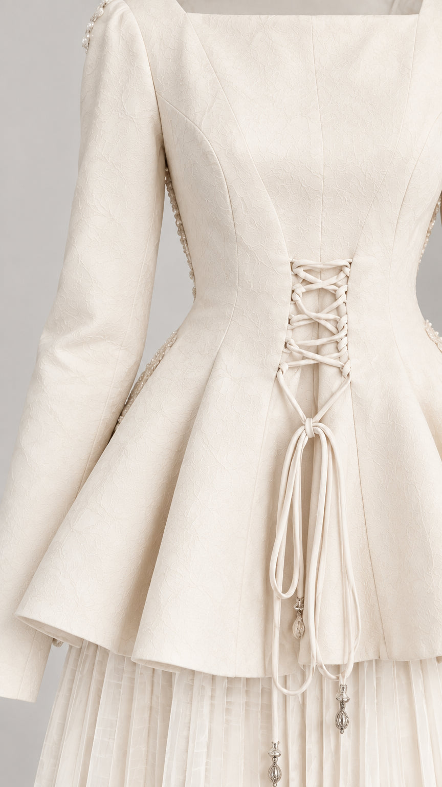 Close up view of the lace-up corset detail and peplum hem on the off-white dress