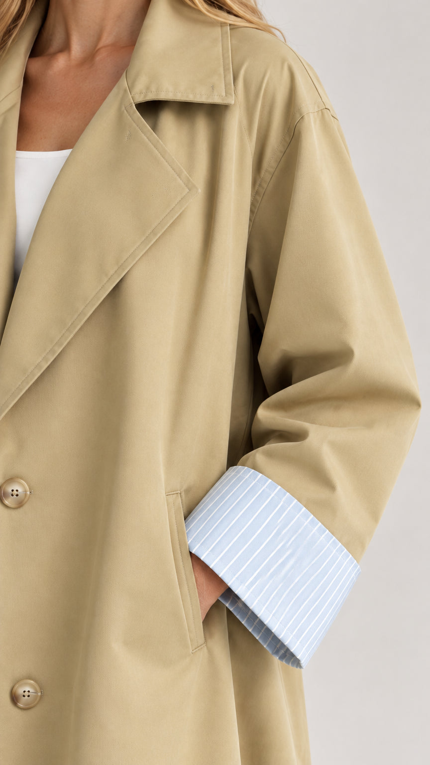 Close-up detail of khaki trench coat collar, front buttons, and striped sleeve cuff