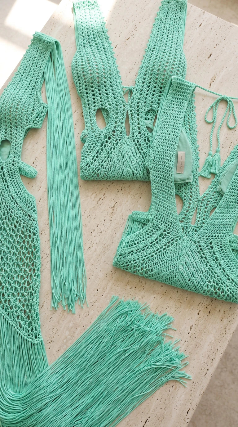 Flat lay detail of mint green crochet knit bodice and long fringe trim