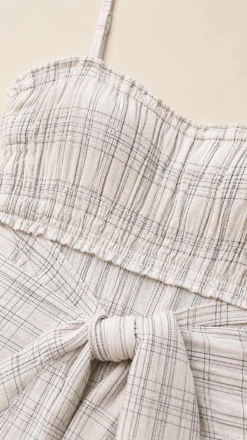 Close-up detail of smocked bodice and tie sash on white plaid dress
