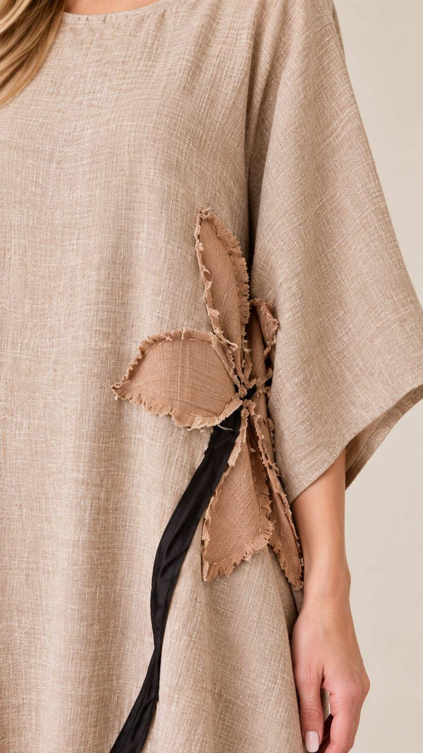 Close-up detail of textured fabric and raw-edge flower appliqué on beige dress