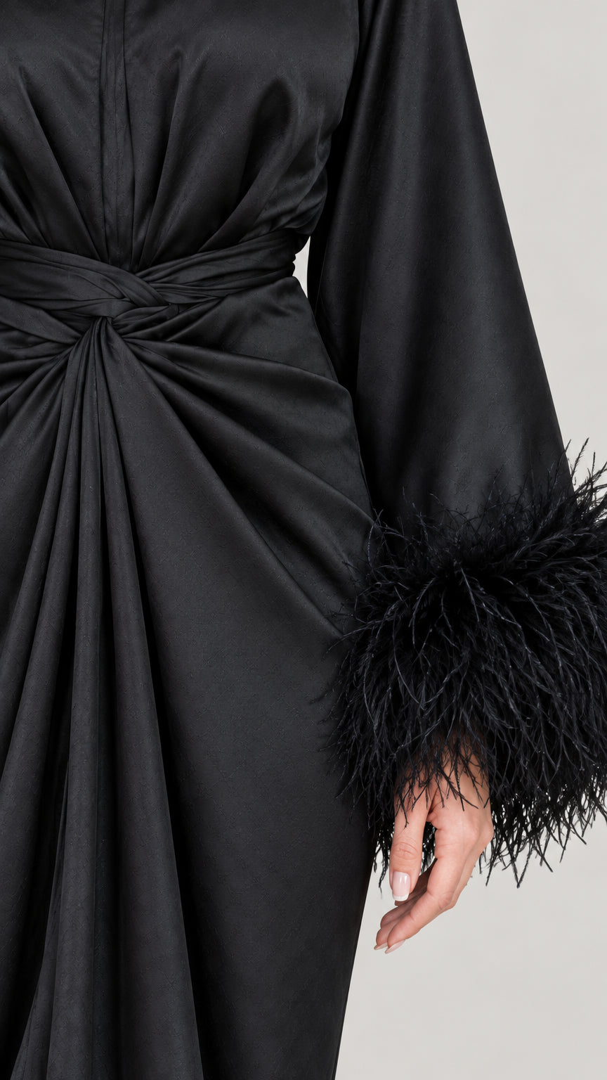 Close-up of twist waist detail and feather-trimmed cuff on black satin dress