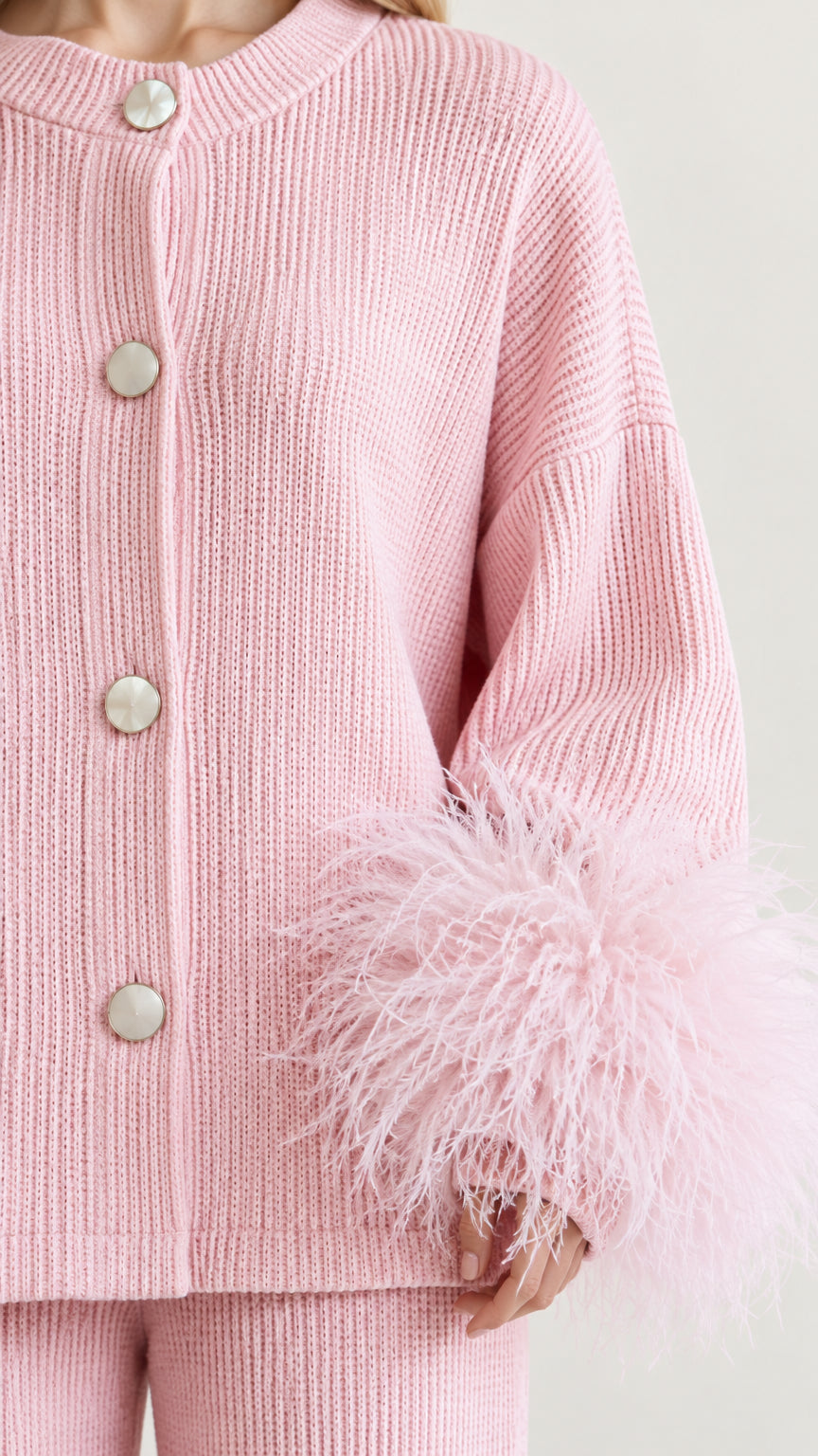 Close-up detail of pink ribbed knit cardigan fabric, buttons, and fluffy feather-trimmed cuffs