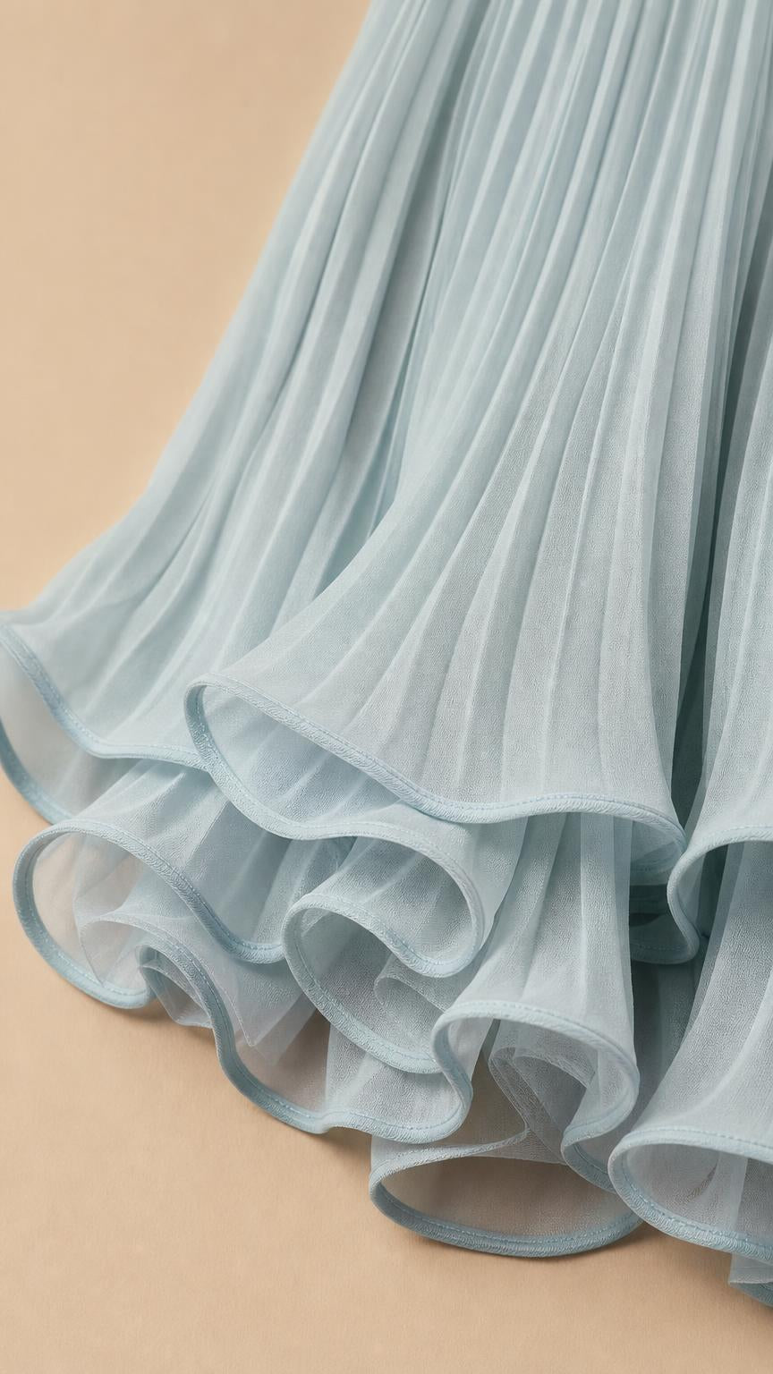Close-up detail of the layered ruffle hem and accordion pleats on sage green dress
