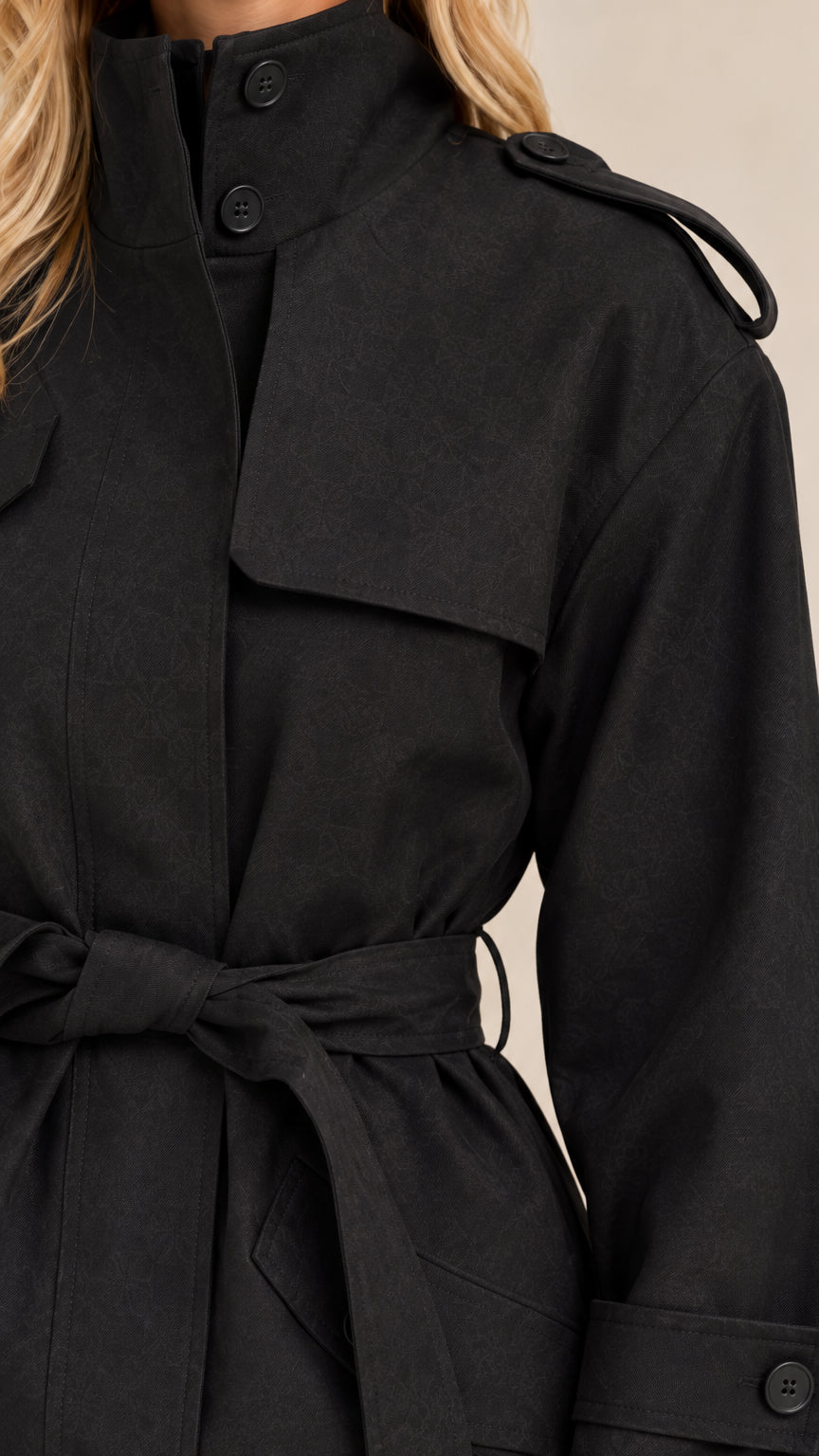 Close-up detail of black short trench coat highlighting stand collar, storm flap, and waist tie