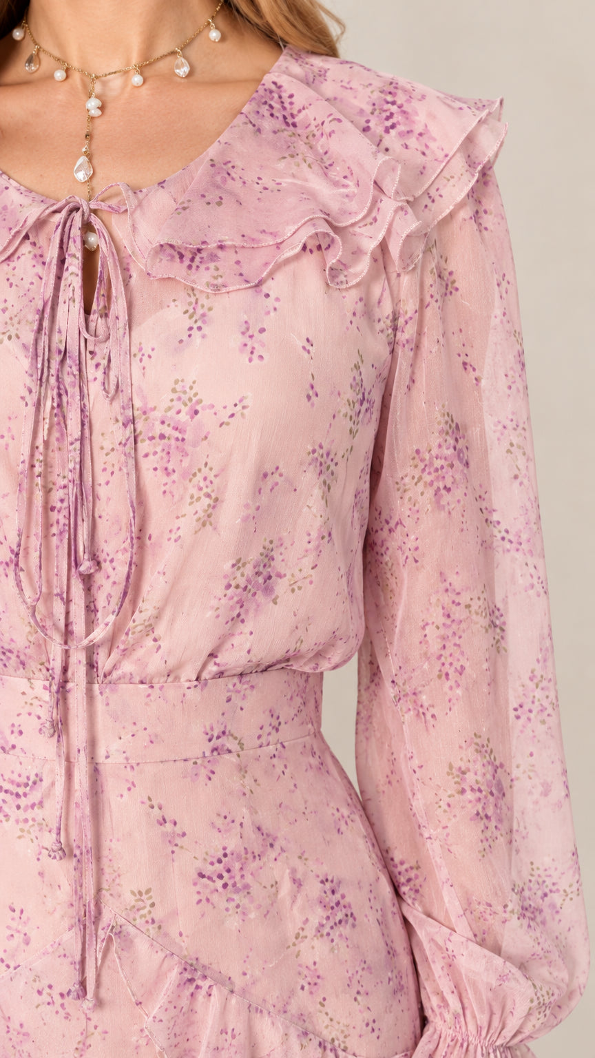 Close-up detail of ruffle tie neckline and floral fabric on blush pink dress