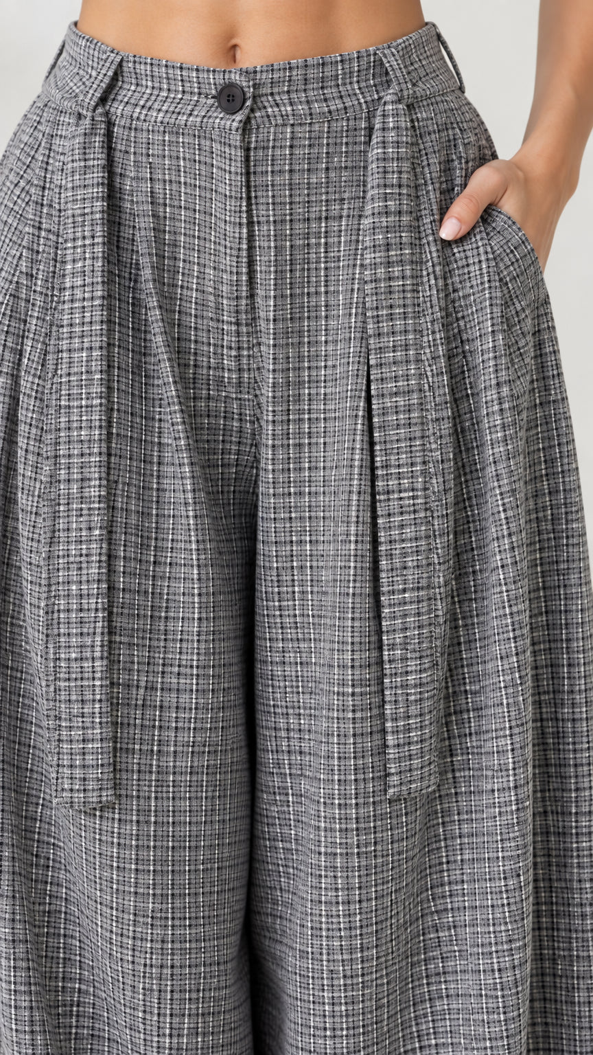 Close up detail of high waist, front pleats, button closure, and pocket on grey plaid pants