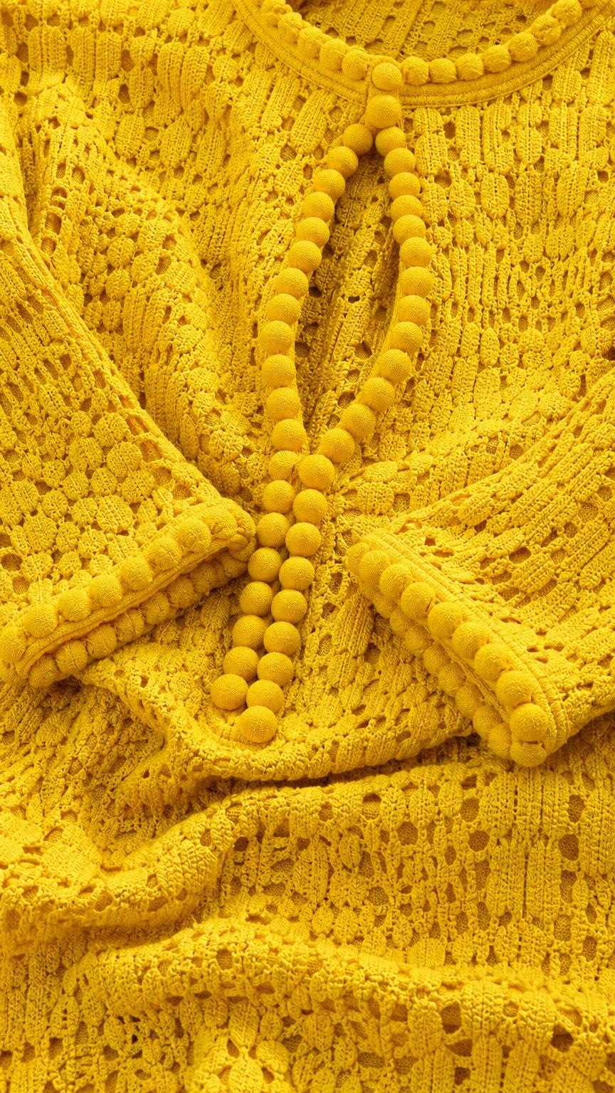 Close-up detail of crochet knit texture and pom-pom buttons