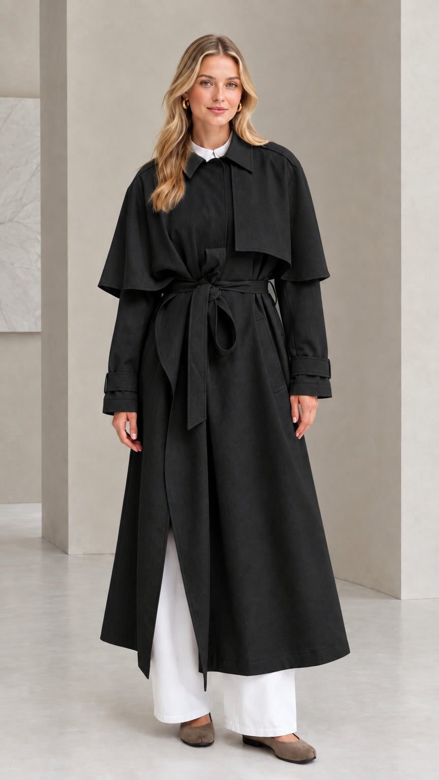 Front full view of black capelet maxi trench coat styled with wide-leg trousers