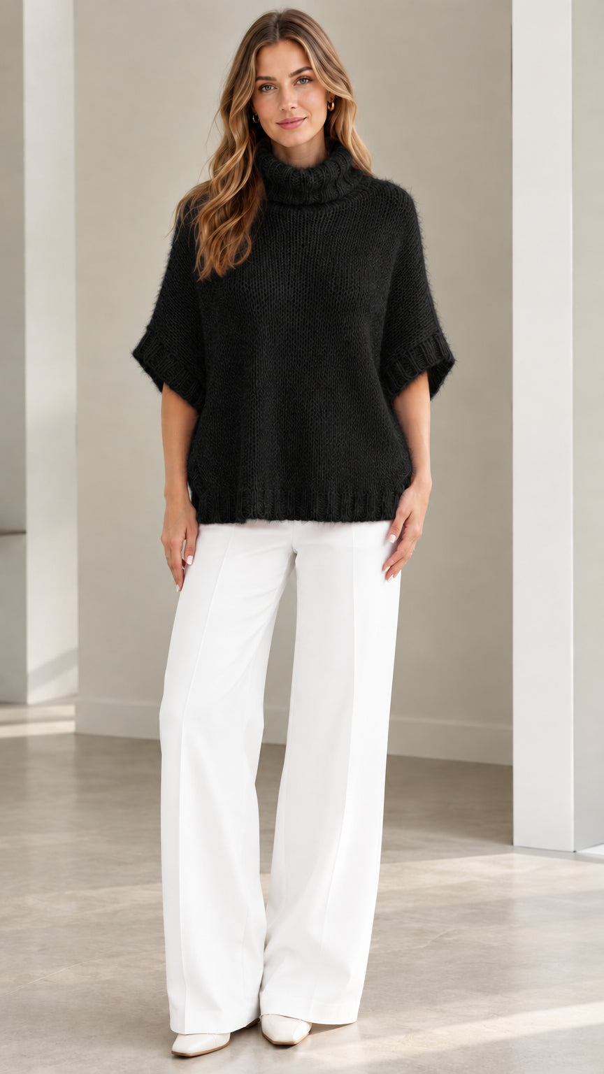 Model wearing Black short sleeve turtleneck poncho knit sweater with white pants