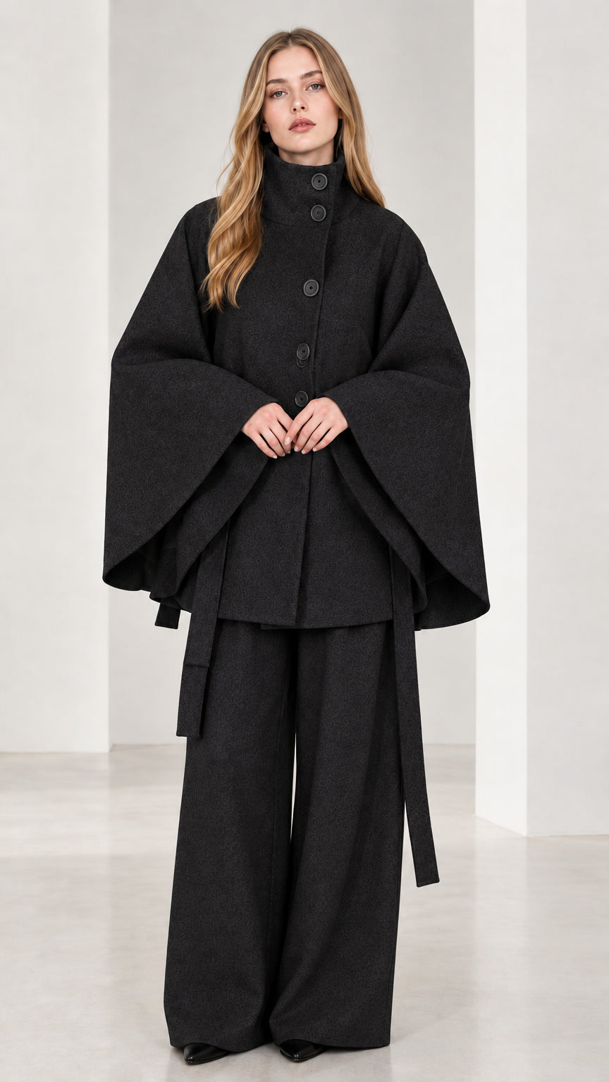Front view of black high neck belted cape coat and wide-leg trousers set