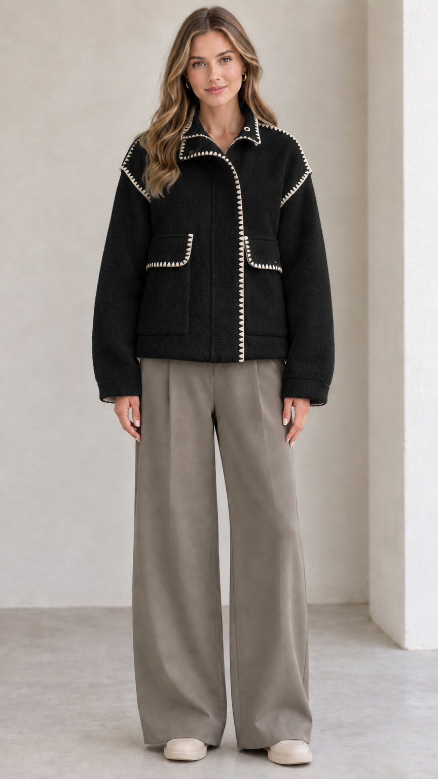Model wearing black fleece jacket with white contrast whipstitch trim
