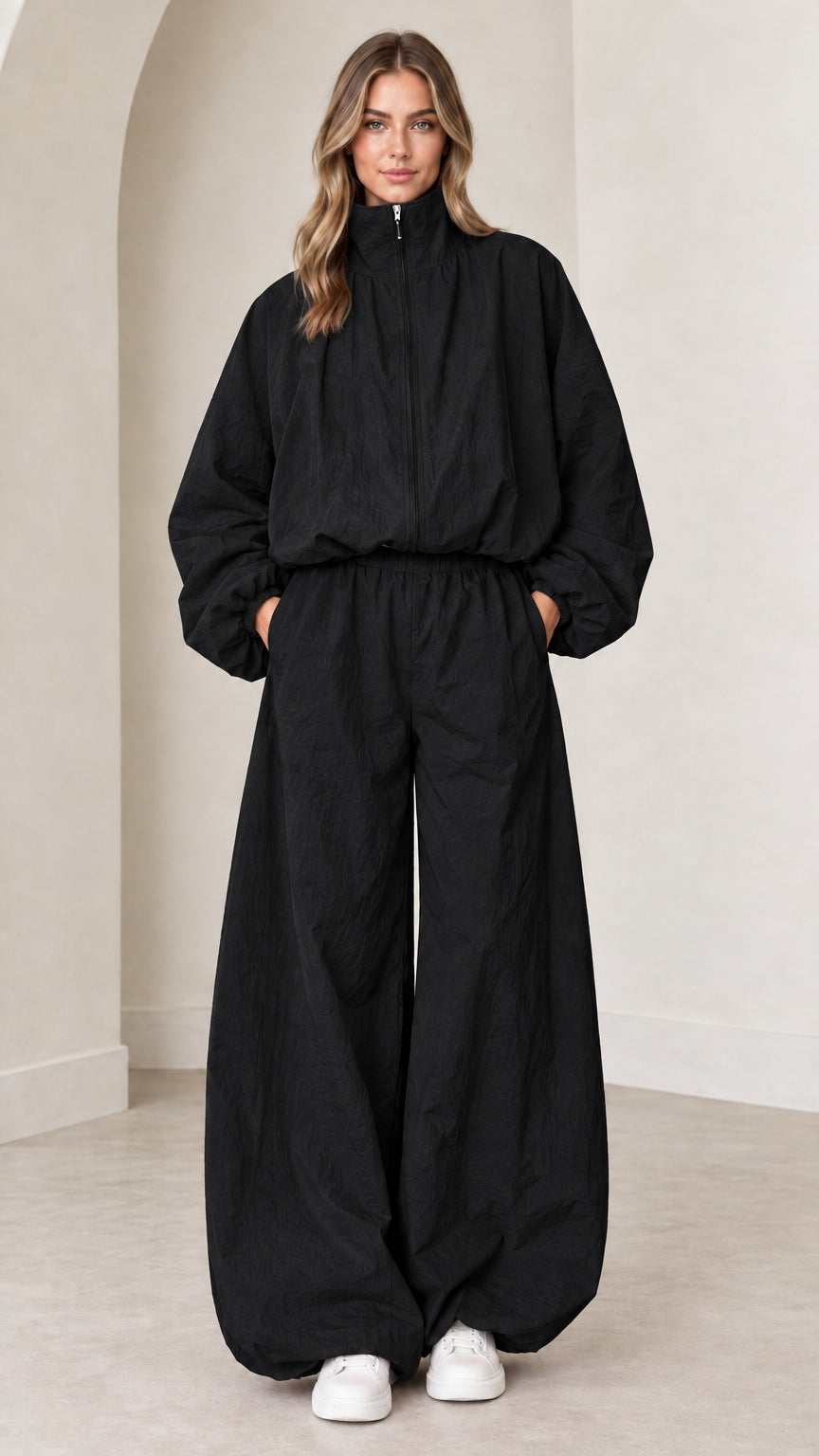 Model wearing black funnel neck wide-leg parachute jumpsuit with white sneakers