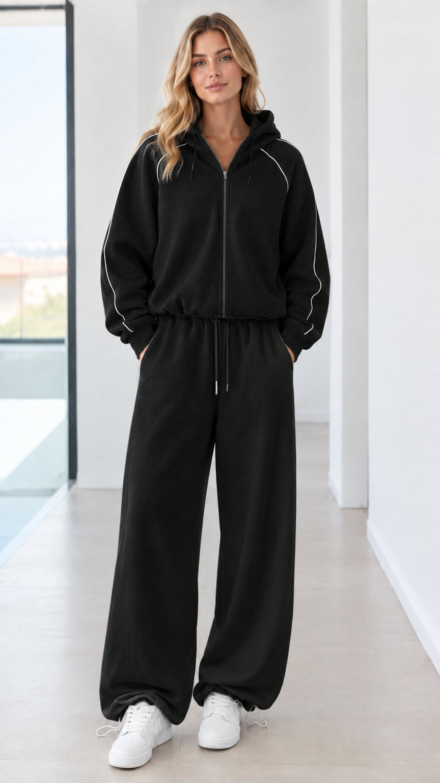 Full body studio shot of model wearing black zip-up hoodie and matching wide-leg sweatpants