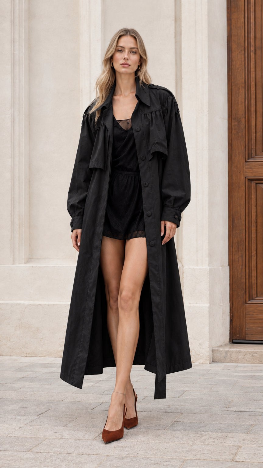 Women's black maxi trench coat styled over black romper and heels
