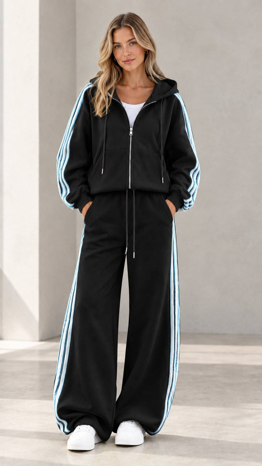 Model wearing black two-piece tracksuit set with light blue side stripes and white sneakers