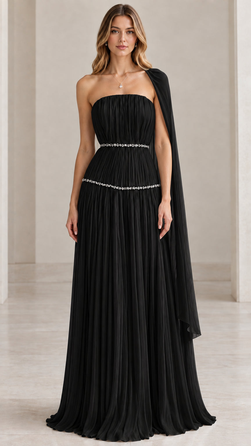 Model wearing black strapless pleated evening gown with attached cape drape and crystal trim
