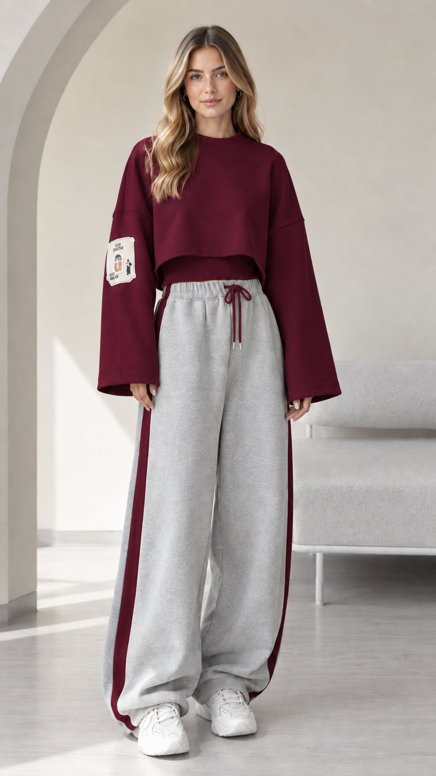 Model wearing burgundy cropped sweatshirt and grey wide leg sweatpants with burgundy side stripe