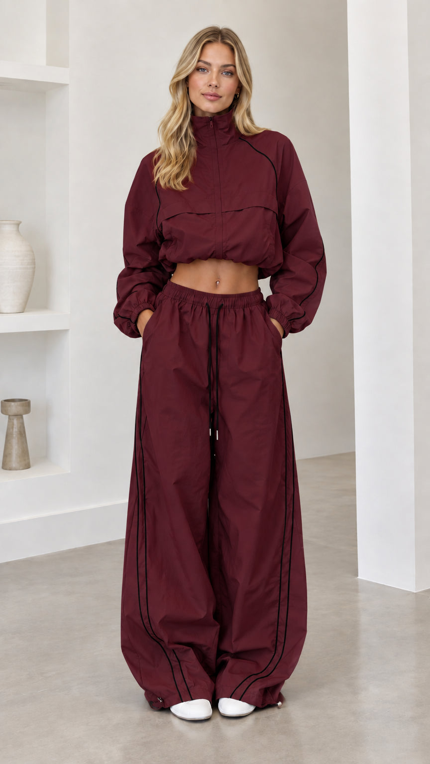 Model wearing burgundy cropped windbreaker and wide-leg track pants set with black piping