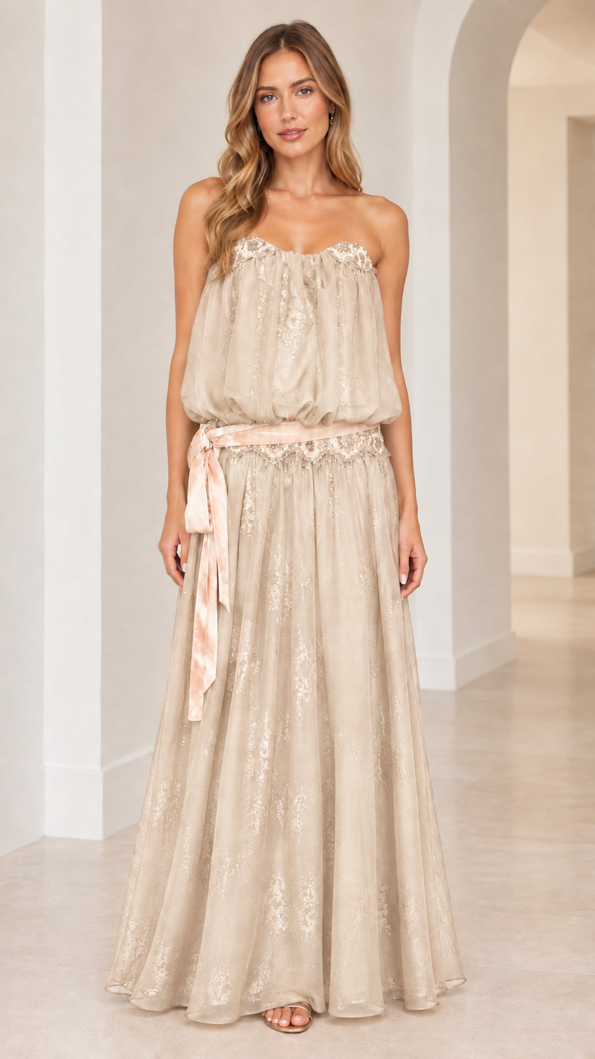Front view of woman wearing strapless champagne beige blouson maxi dress with sash